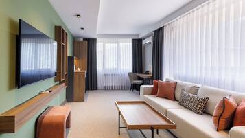 Una sala de estar moderna con televisor de pantalla plana, un sofá con cojines estampados, una mesa de centro de madera y una zona de comedor con una silla y una mesa.