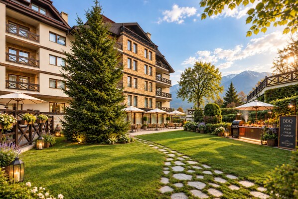 A hotel courtyard with a stone pathway, outdoor seating, and a BBQ area.