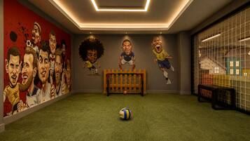 A room with a soccer-themed mural, a goalpost, and a soccer ball on artificial turf.