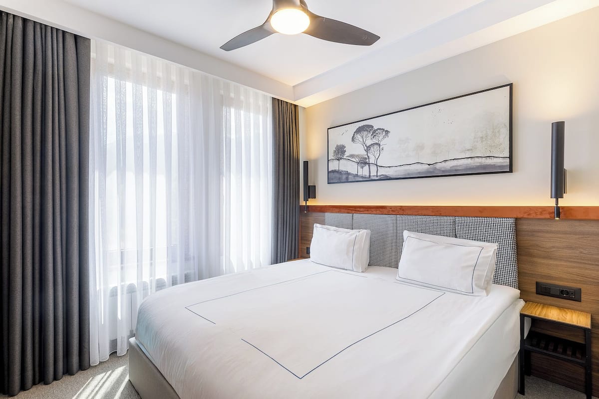 A modern hotel room with a large bed, a ceiling fan, and a painting on the wall.