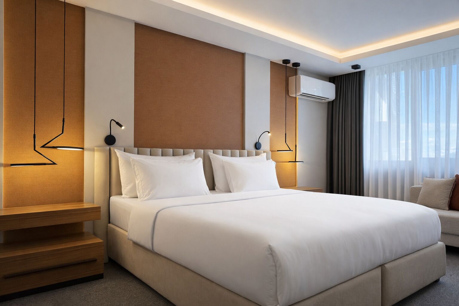Una habitación de hotel moderna con una cama grande, una mesita de noche, aire acondicionado integrado y vistas al exterior a través de cortinas translúcidas.