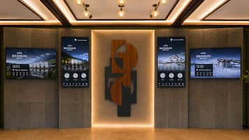 Een receptiegedeelte met een centraal logo en drie digitale schermen die informatie over het hotel tonen.