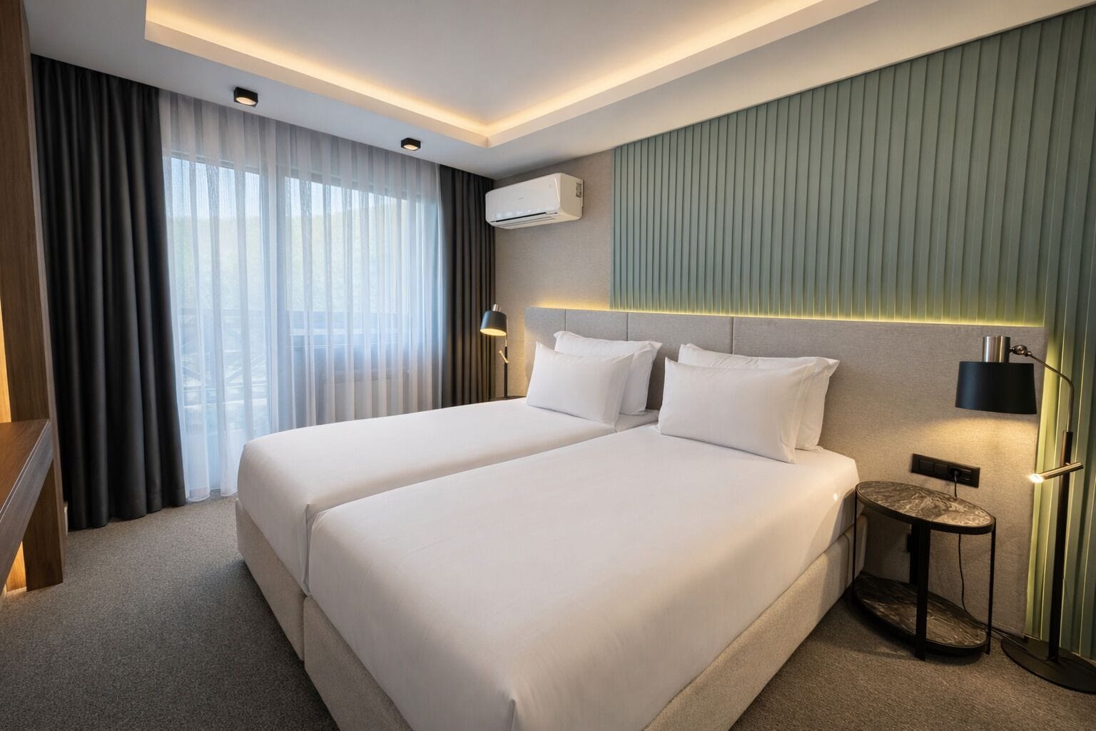 Ett hotellrum med två sängar, en golvlampa, en luftkonditioneringsanläggning och utsikt över omgivningarna genom tunna gardiner.