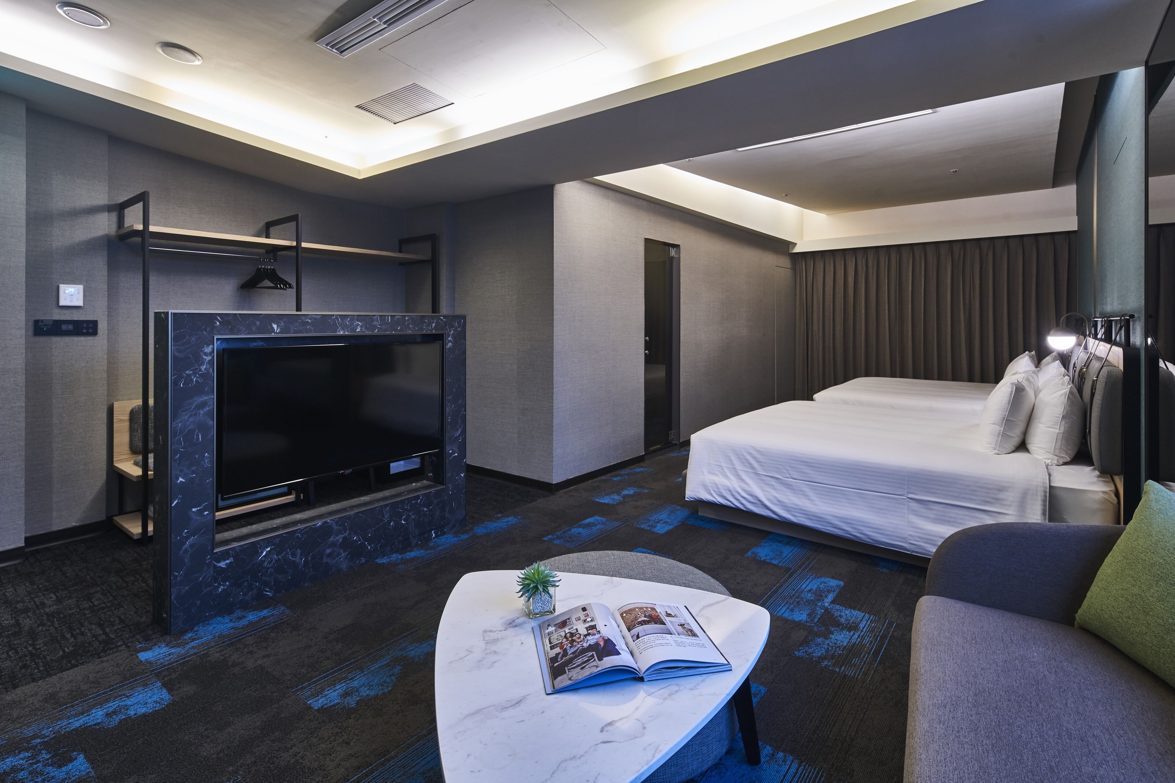 Una habitación de hotel moderna con una cama grande, un televisor de pantalla plana, una mesita de centro de mármol y una planta pequeña.