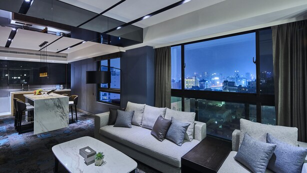 Un salón moderno con sofá, mesa de centro y vistas a la ciudad a través de amplias ventanas.