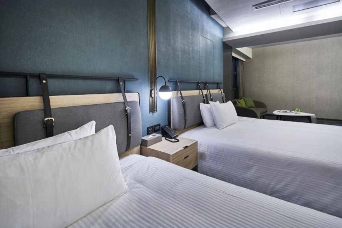 A hotel room with two beds, bedside tables, lamps, and a small table with a green object on it.