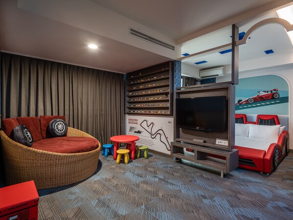 A room with a large flat-screen TV, a red sofa, a wicker chair, a small table, and a wall with a racing car mural.