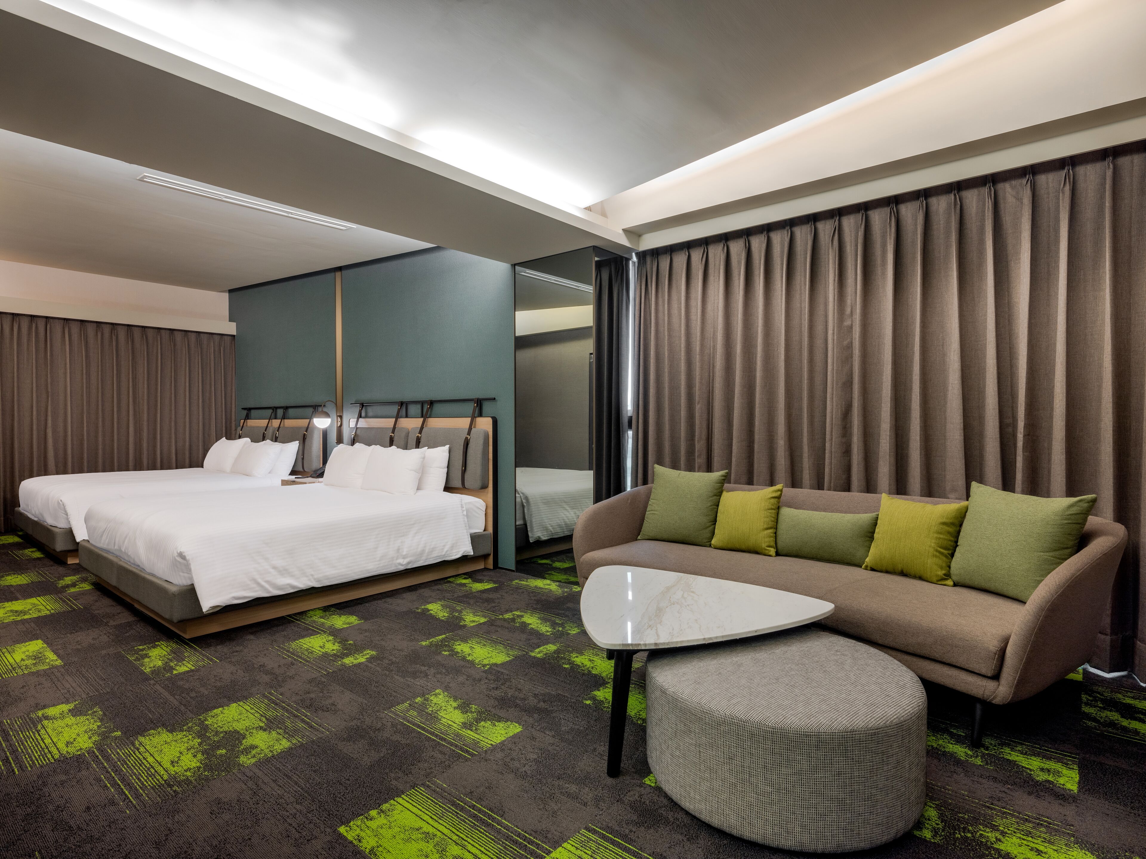 Une chambre d’hôtel avec un grand lit, un canapé, une table basse et un petit pouf.