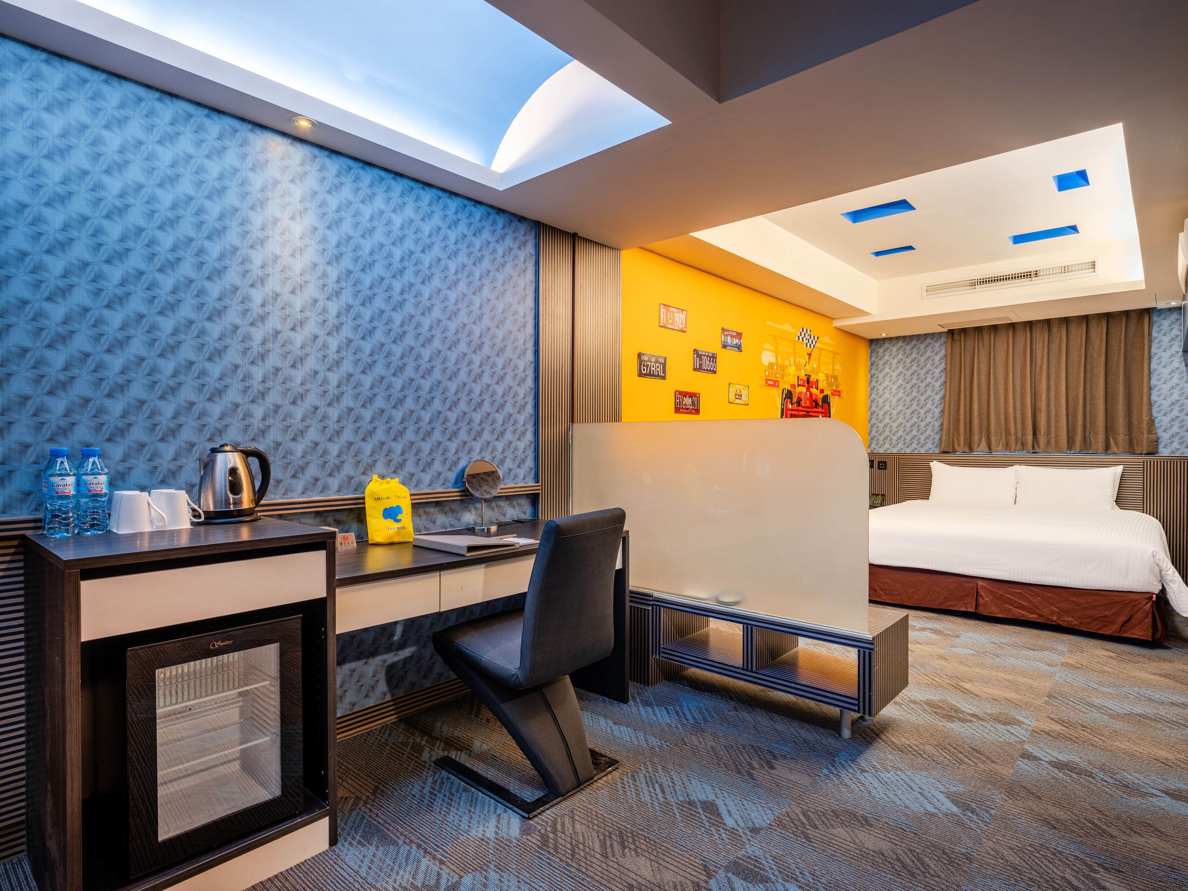 A hotel room with a desk, chair, bed, and a large window.