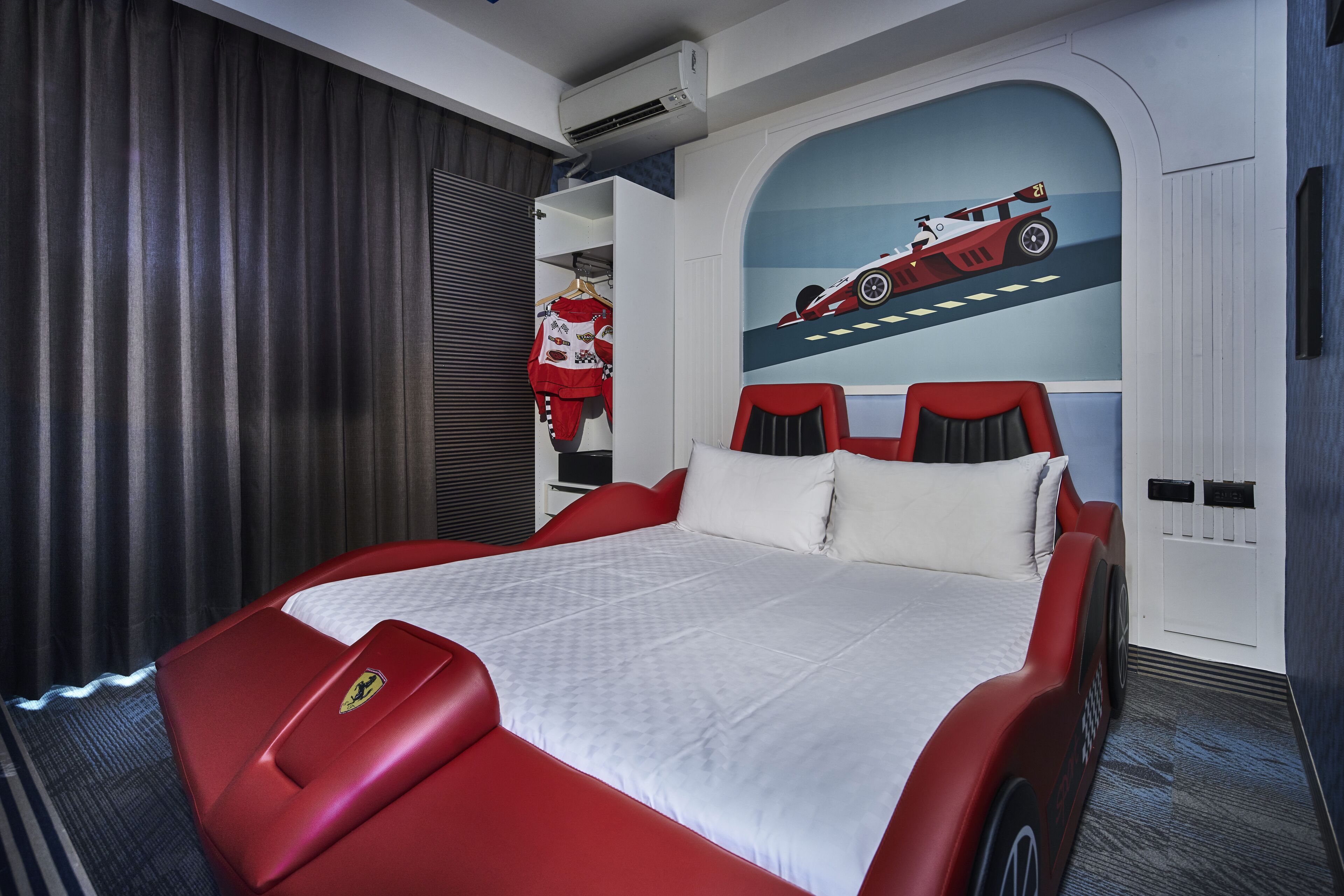 A bedroom with a large bed, a red Ferrari logo on the headboard, a racing car mural on the wall, and a wardrobe with a red and white theme.