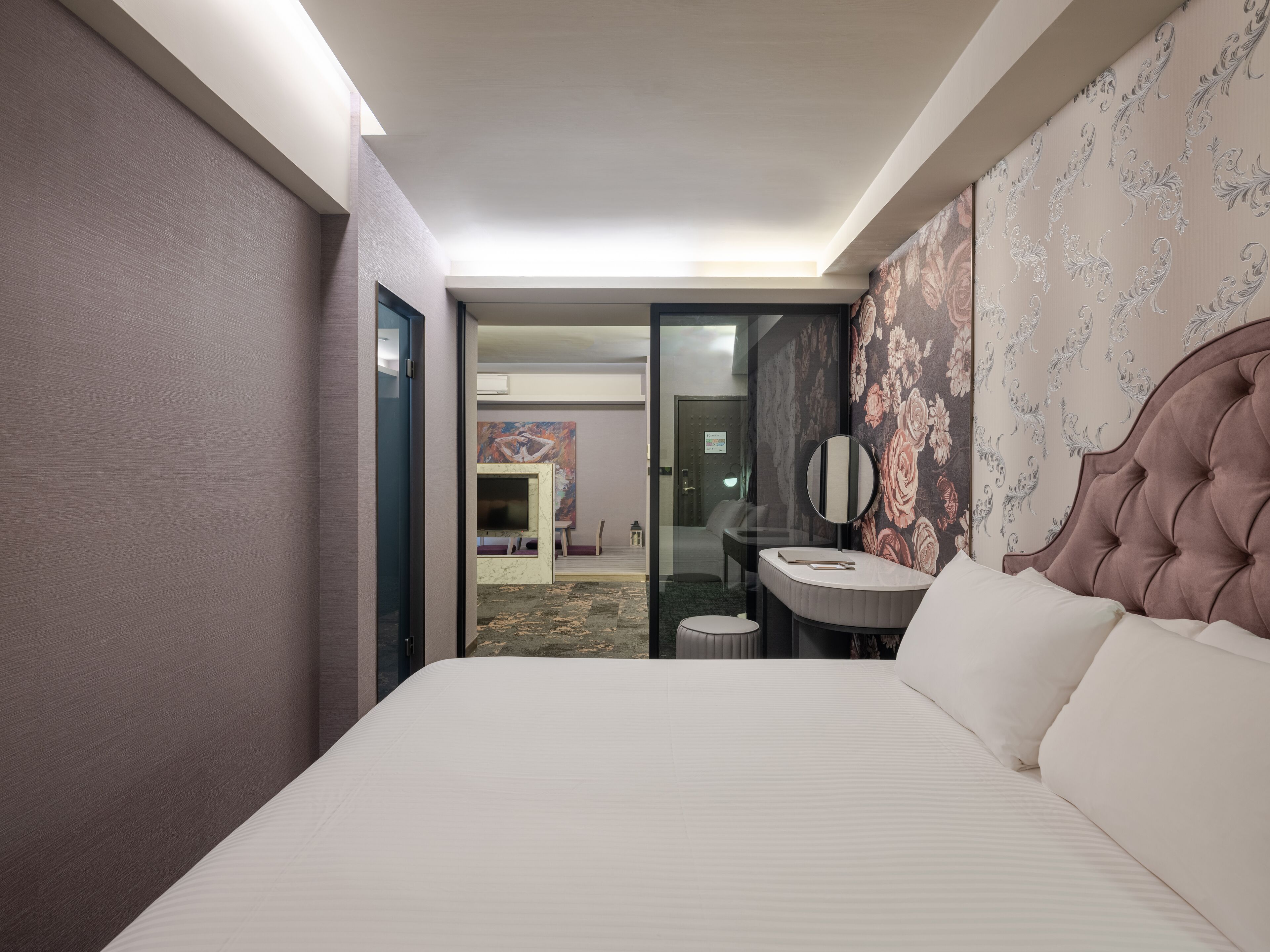 A hotel room with a large bed, a small round table with a mirror, and a bathroom visible through an open door.