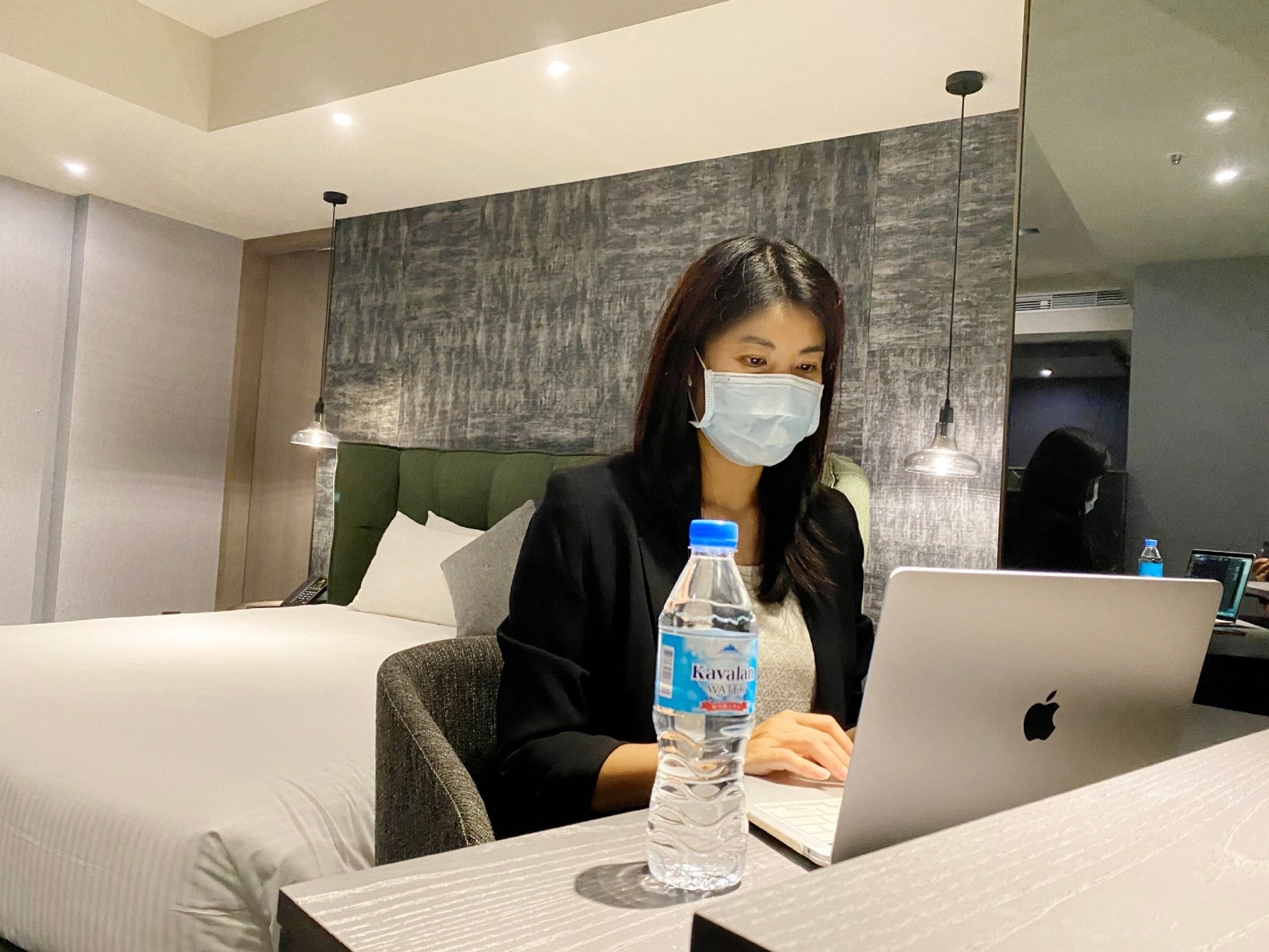 A hotel room with a bed, a laptop, and a bottle of water on the table.
