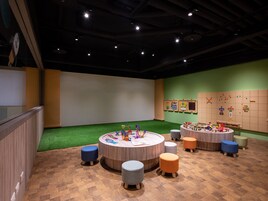 Un'area giochi per bambini con tavoli rotondi, giocattoli colorati e una parete con il gioco dell'incastro.