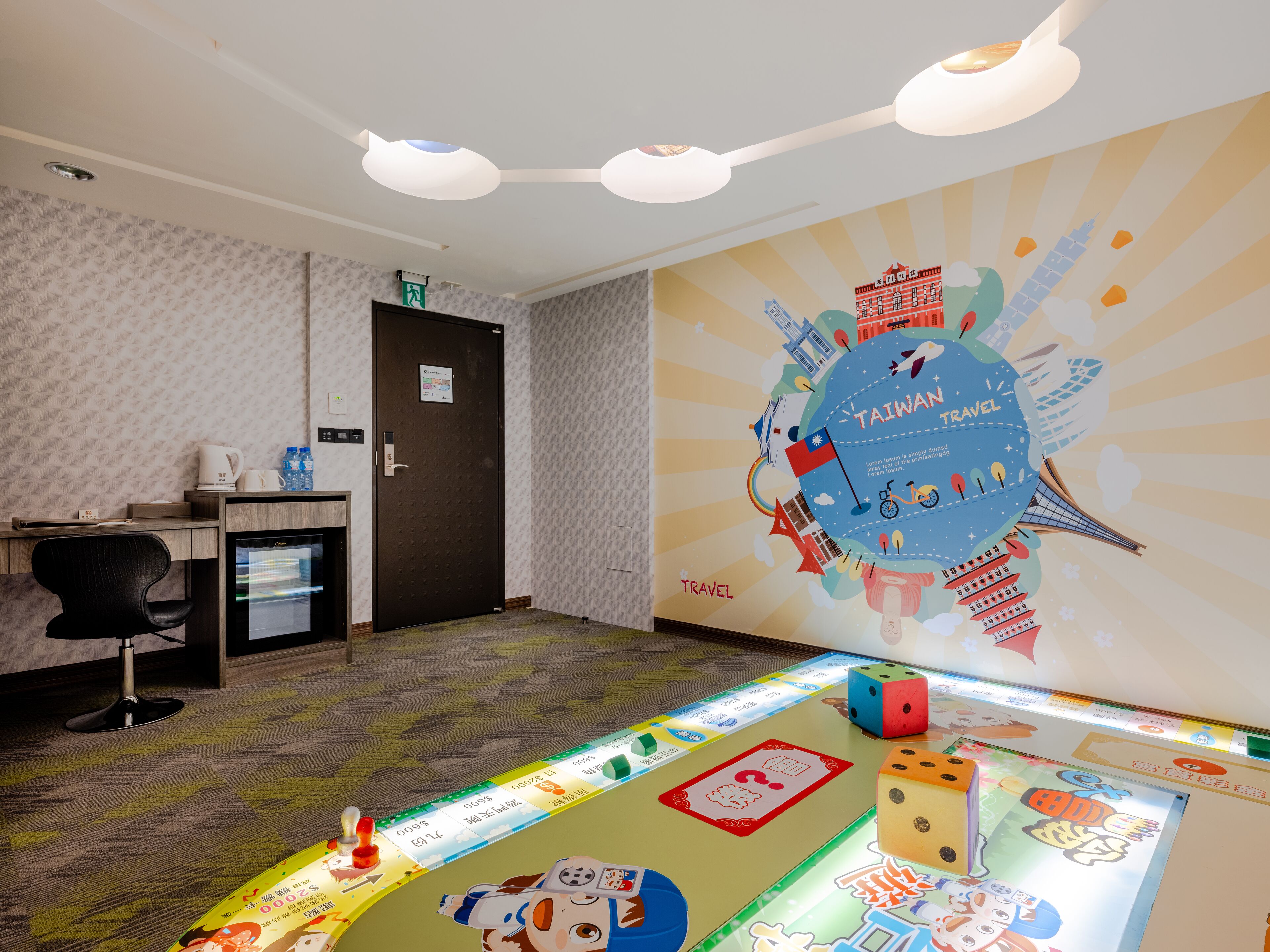 Een hotelkamer met een bureau, een stoel, een minibar en een muur met een thematisch schilderwerk over reizen.