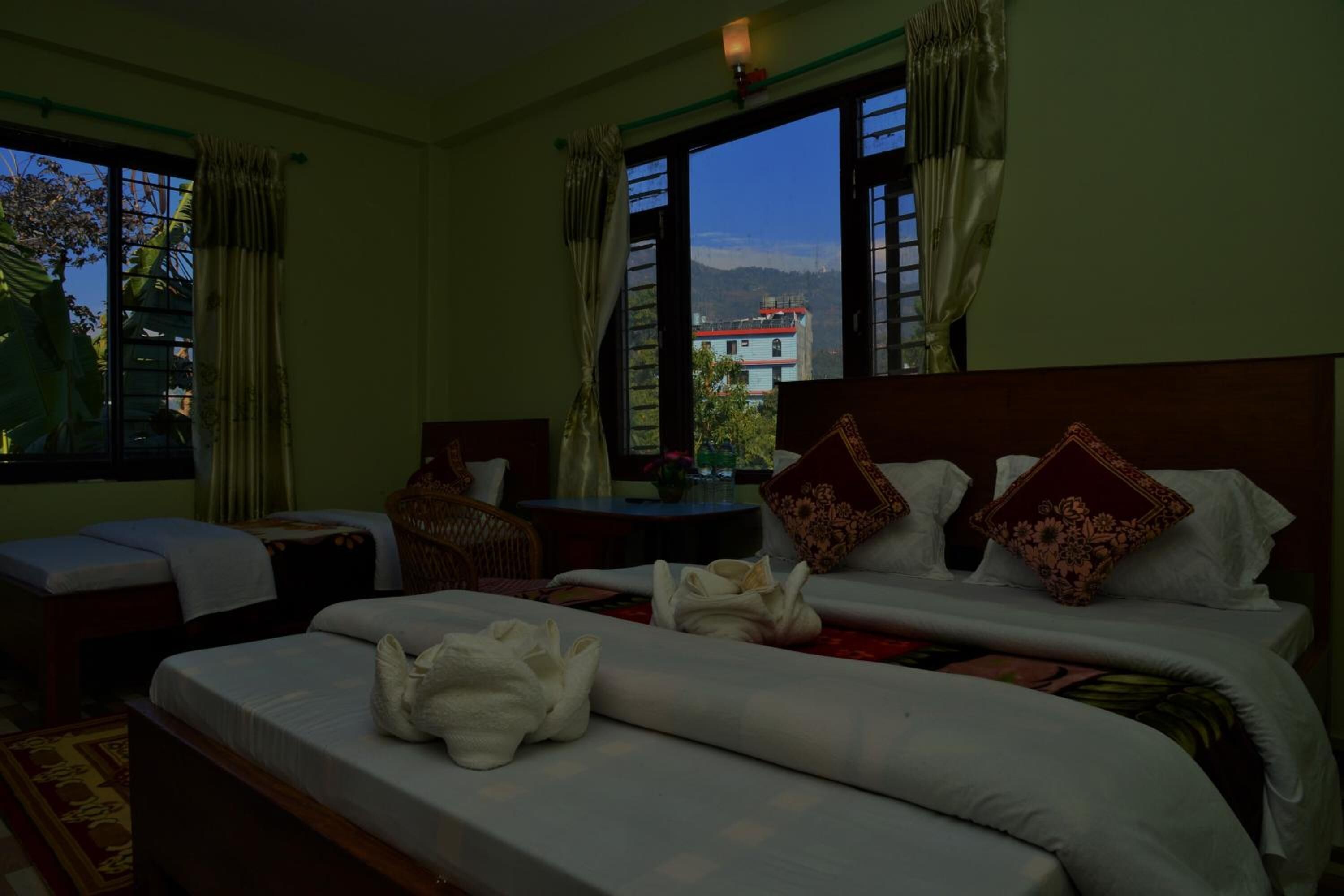 A hotel room with a large bed, a smaller bed, a table, and a window with a view of mountains.