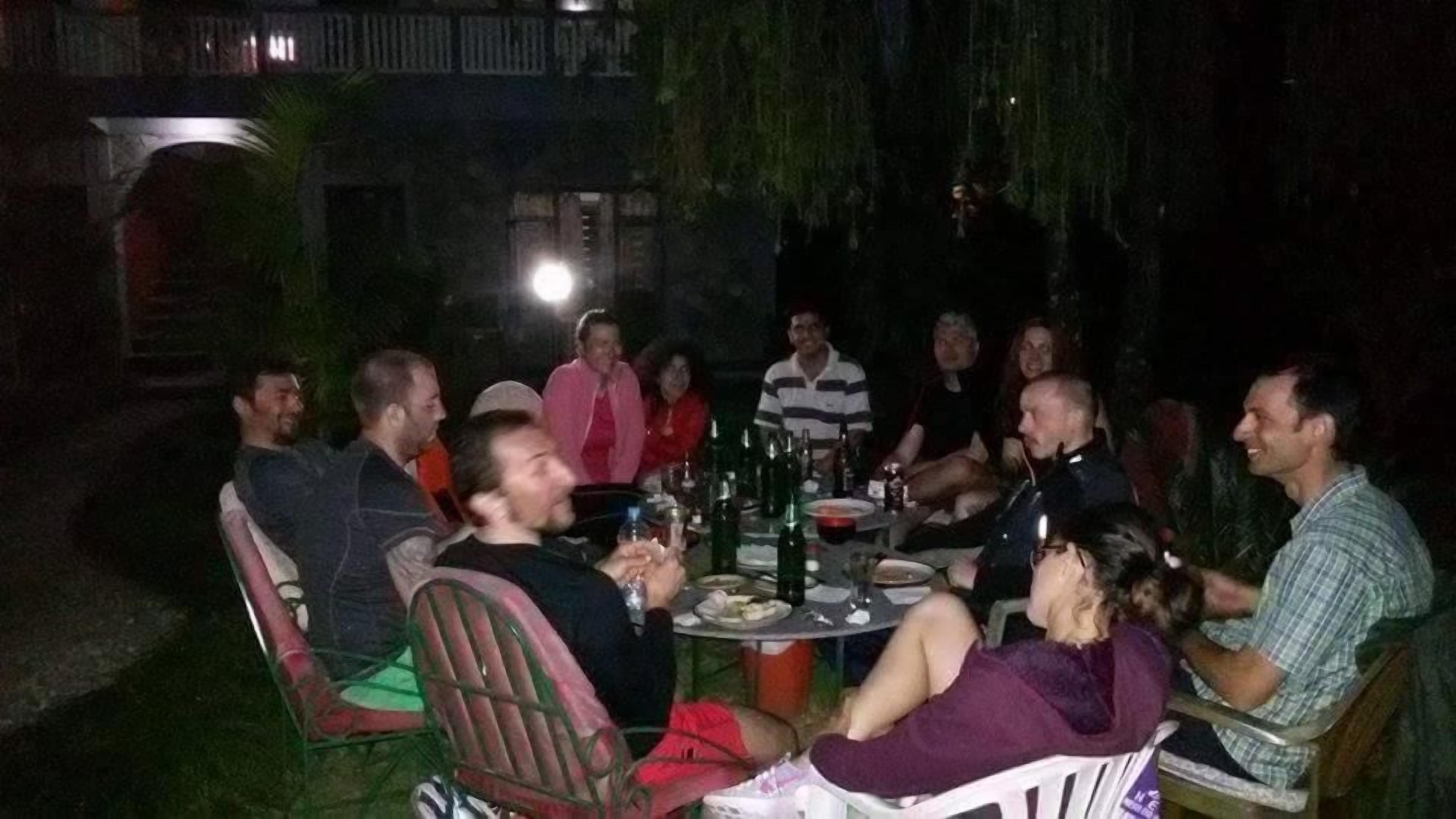 Un groupe de personnes est assis autour d’une table à l’extérieur, la nuit.