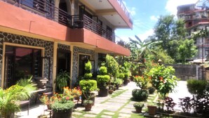 A two-story building with a balcony, surrounded by a well-maintained garden with various plants and flowers. - Hotel Mandala (Pokhara)