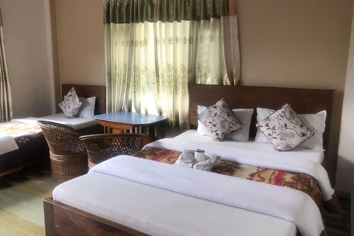 A hotel room with a bed, a small table, a chair, and a window with curtains.