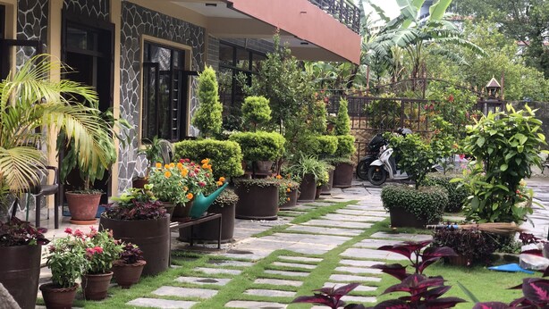 A garden area with potted plants, a stone pathway, and a building with a balcony. - Hotel Mandala (Pokhara)