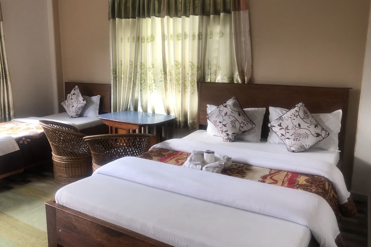 A hotel room with a large bed, a smaller bed, a wooden table, wicker chairs, and a large window with curtains.