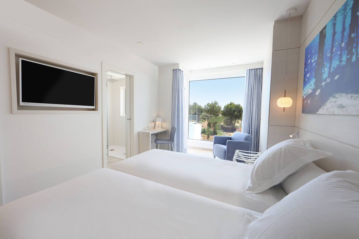 A hotel room with a large bed, a desk, a chair, and a TV mounted on the wall.