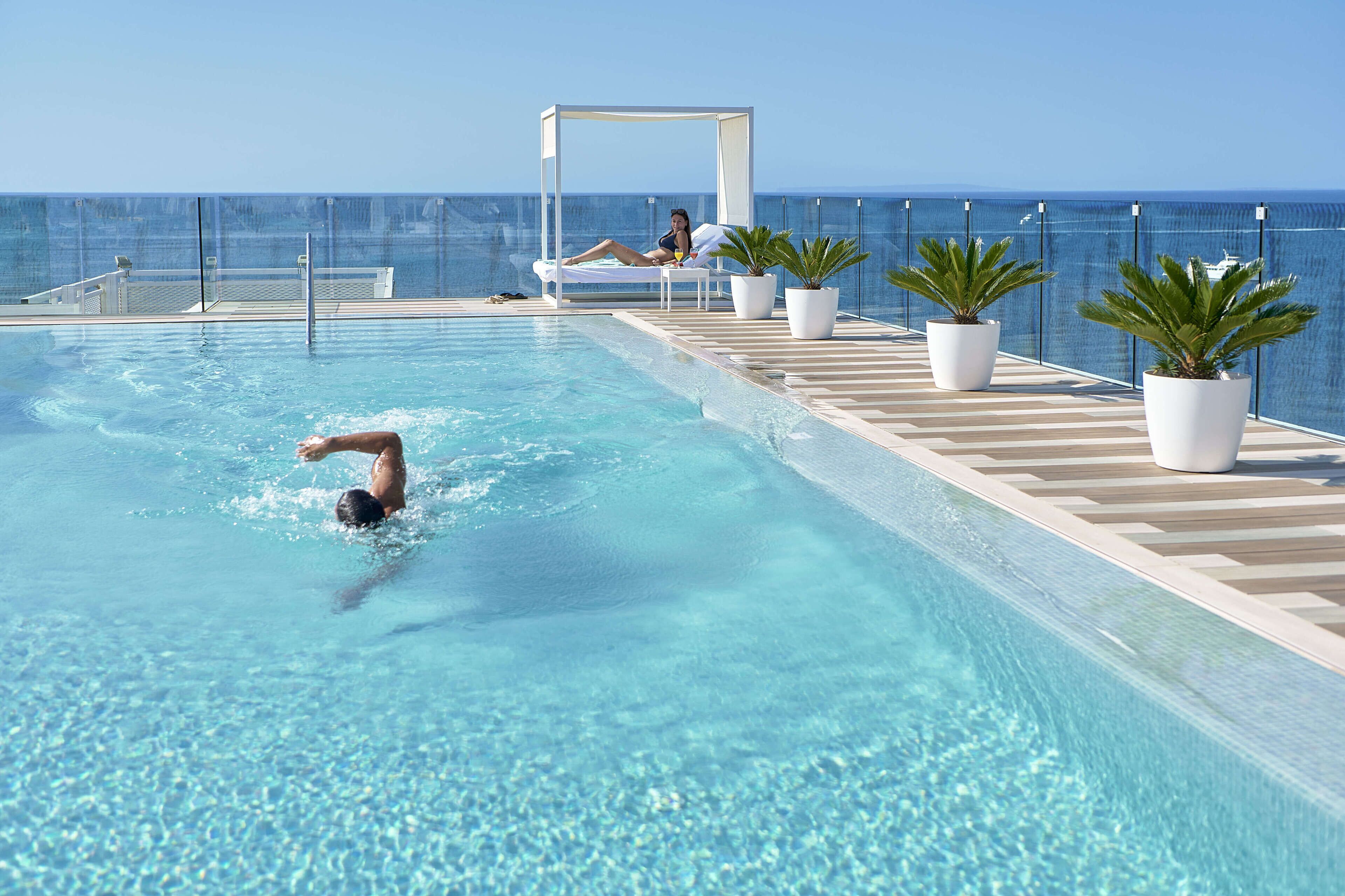 A pool area with a person swimming, a lounging area with a canopy, and potted plants.