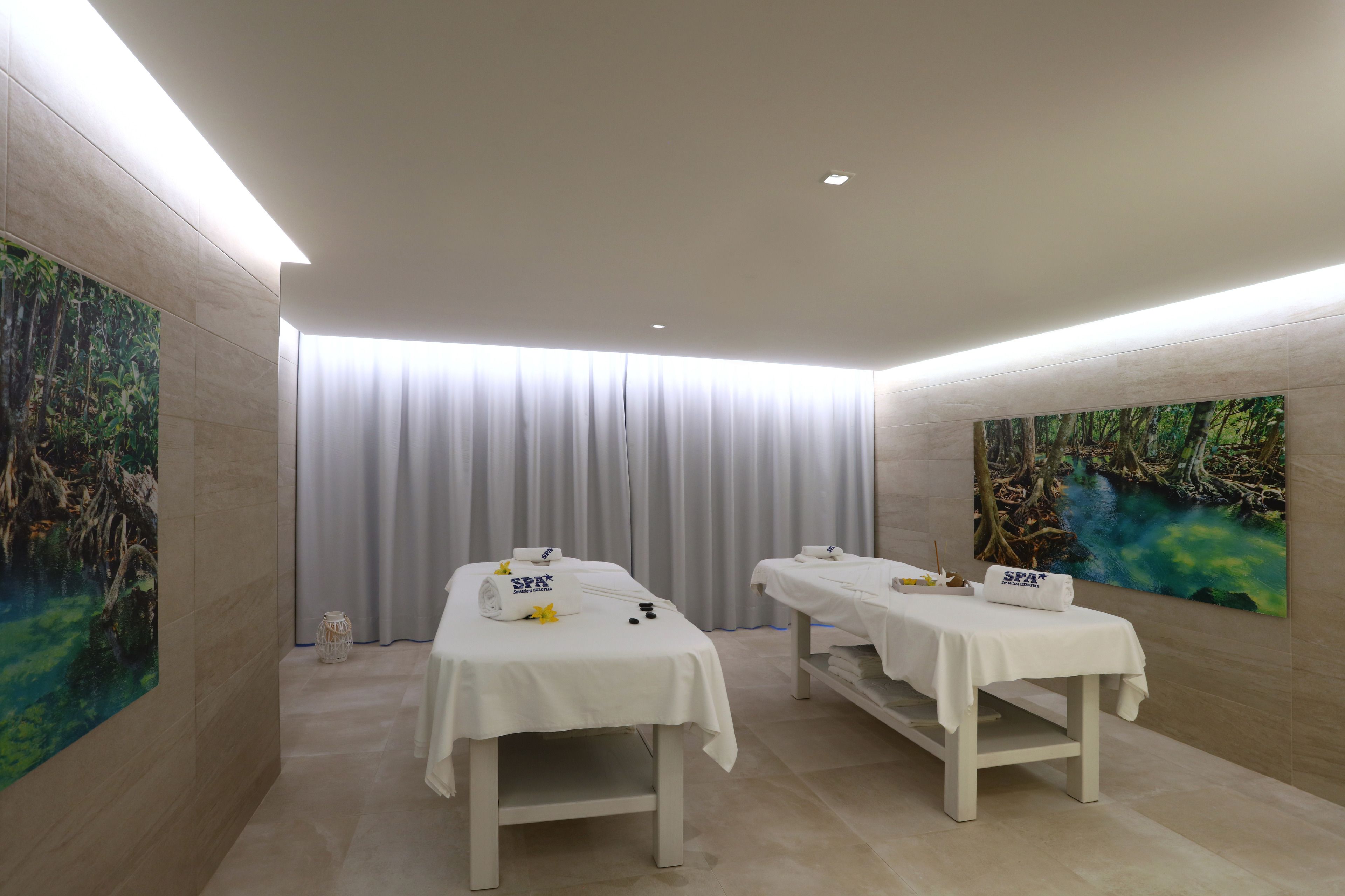 Un cuarto de spa con dos camillas, un ventanal con cortinas y obras de arte en las paredes.
