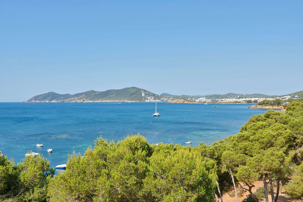 A coastal view with boats, clear blue sea, and green hills in the background.