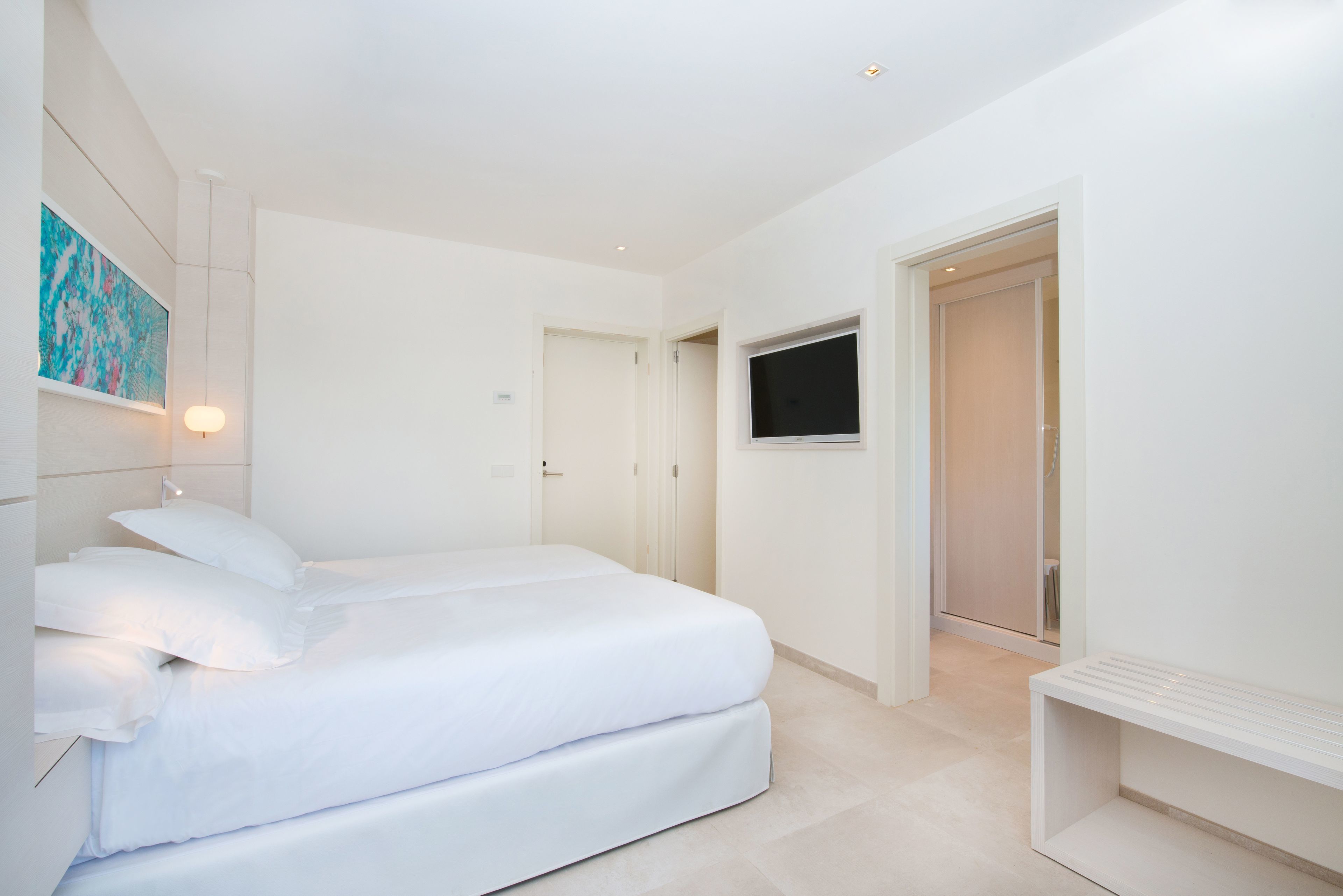 Un dormitorio moderno con una cama, un televisor montado en la pared y una puerta que da a otra habitación.