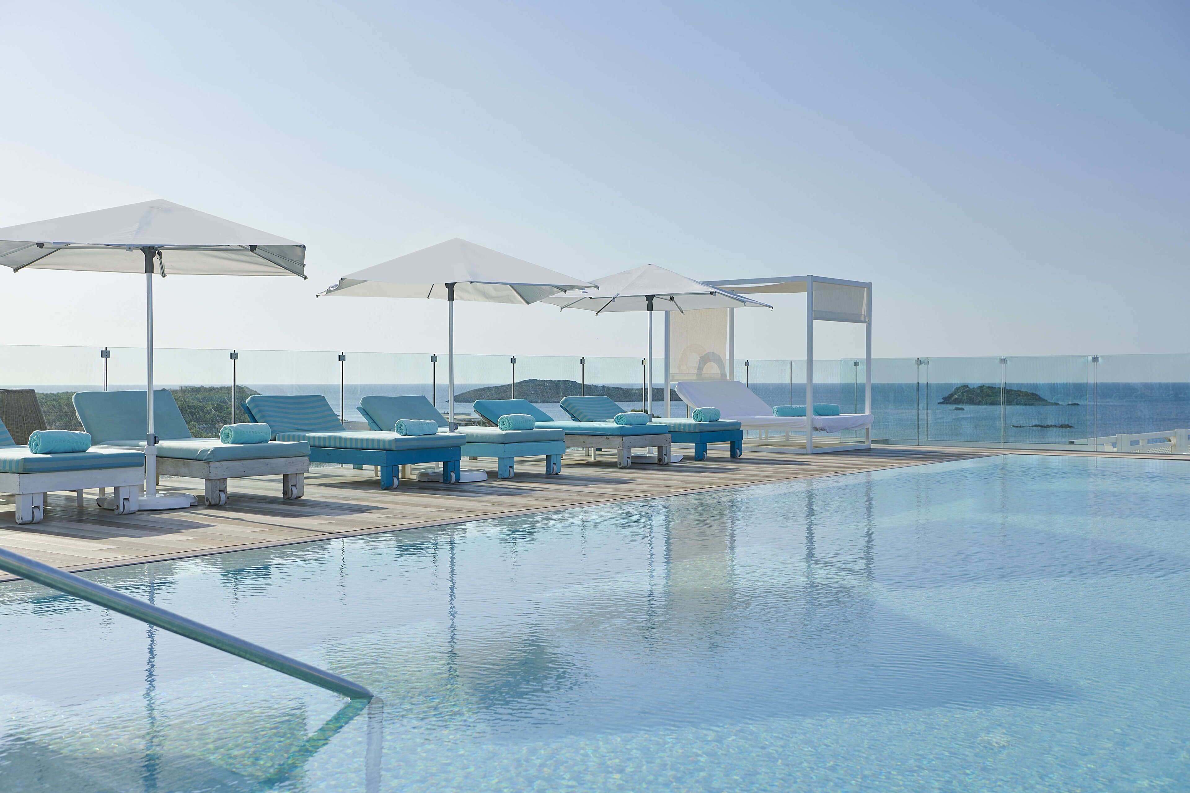 Ein Poolbereich mit Liegestühlen und Sonnenschirmen mit Blick auf klares Wasser.