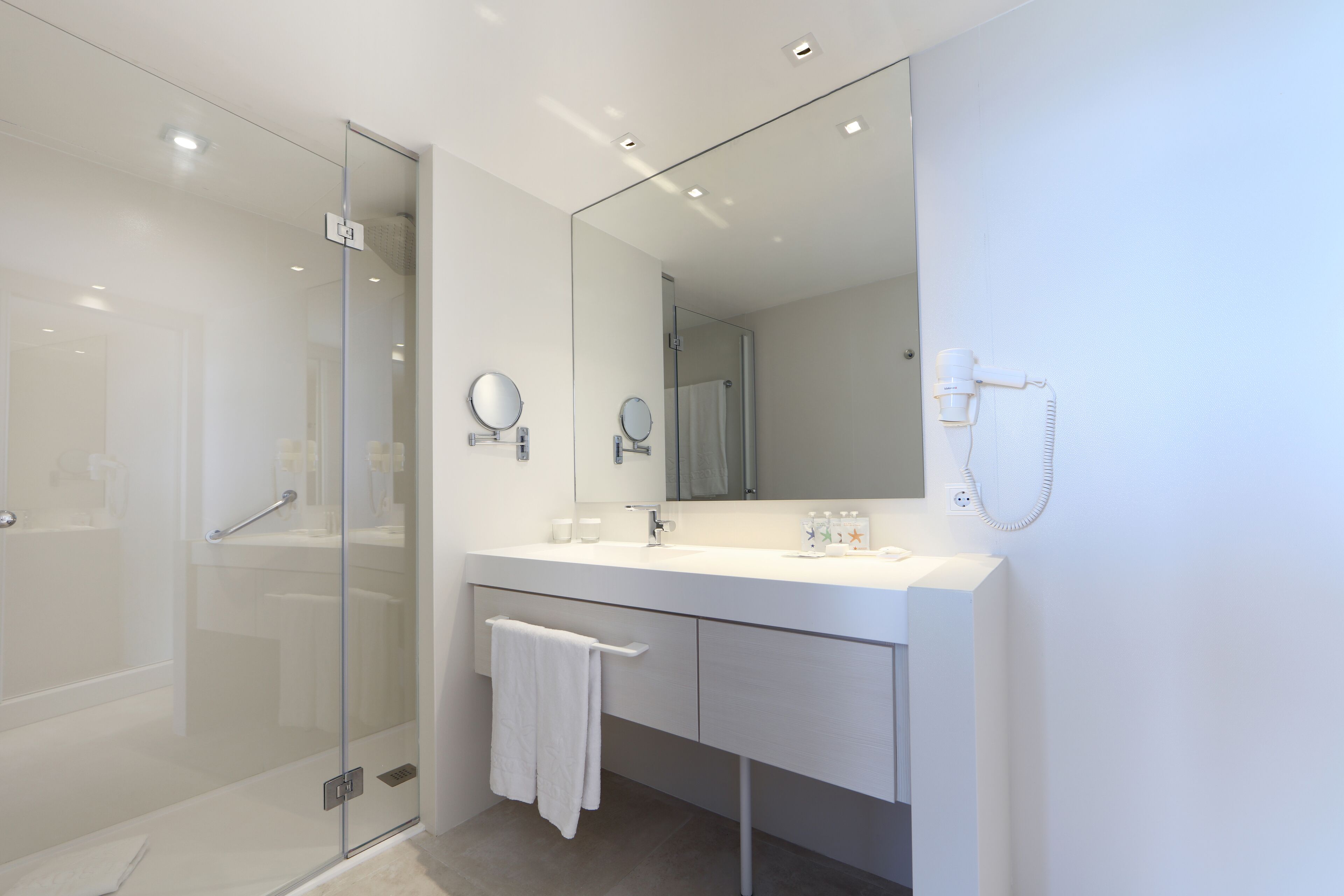 A modern bathroom with a glass shower enclosure, a white vanity with a large mirror, and a towel hanging on the wall.