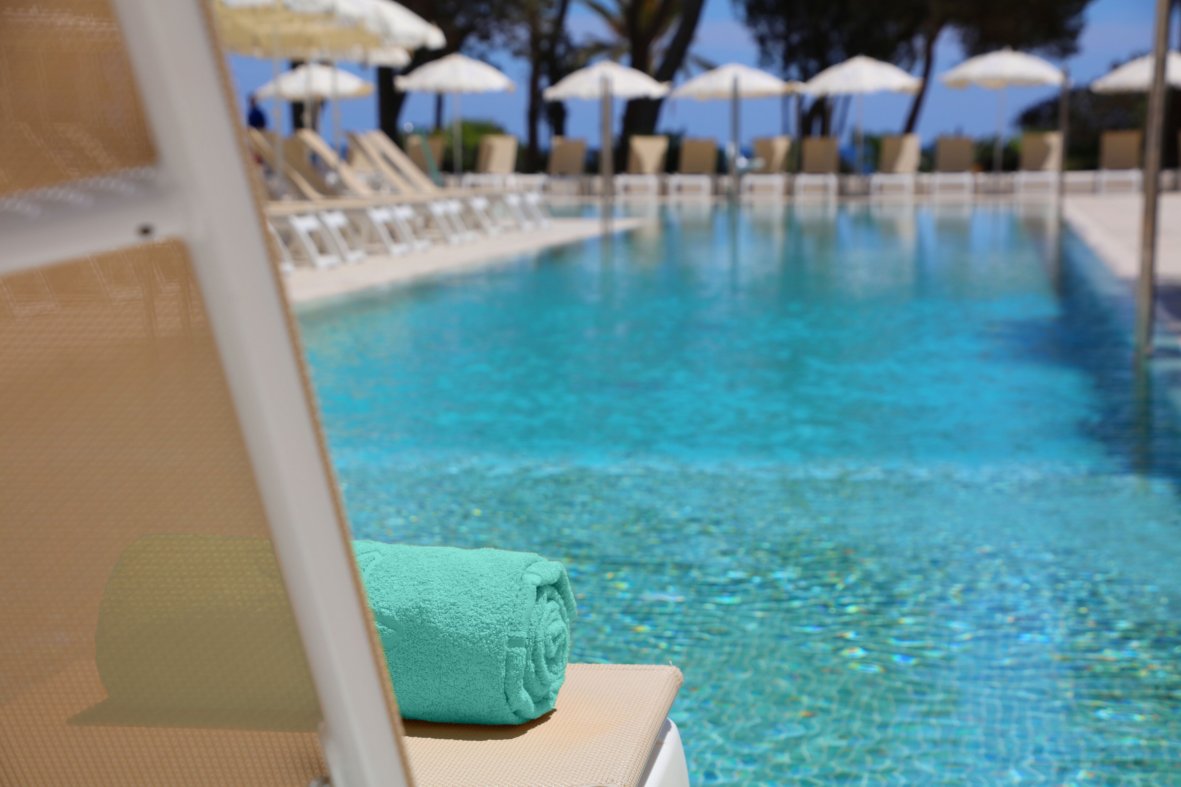 Vista despejada de una piscina con sillones de descanso y sombrillas al fondo.