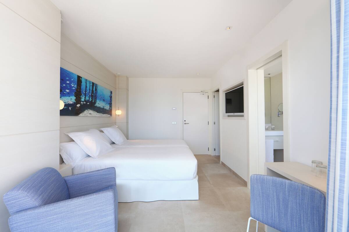 A modern hotel room with a bed, a seating area, and a bathroom visible through an open door.