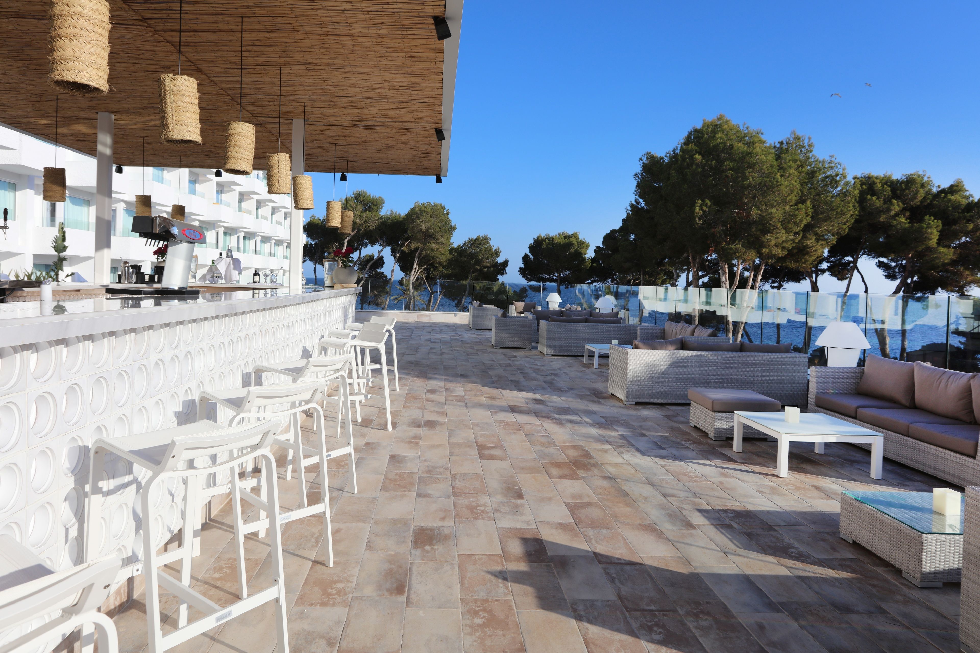 An outdoor seating area with white bar stools, a white table, and a wicker sofa.