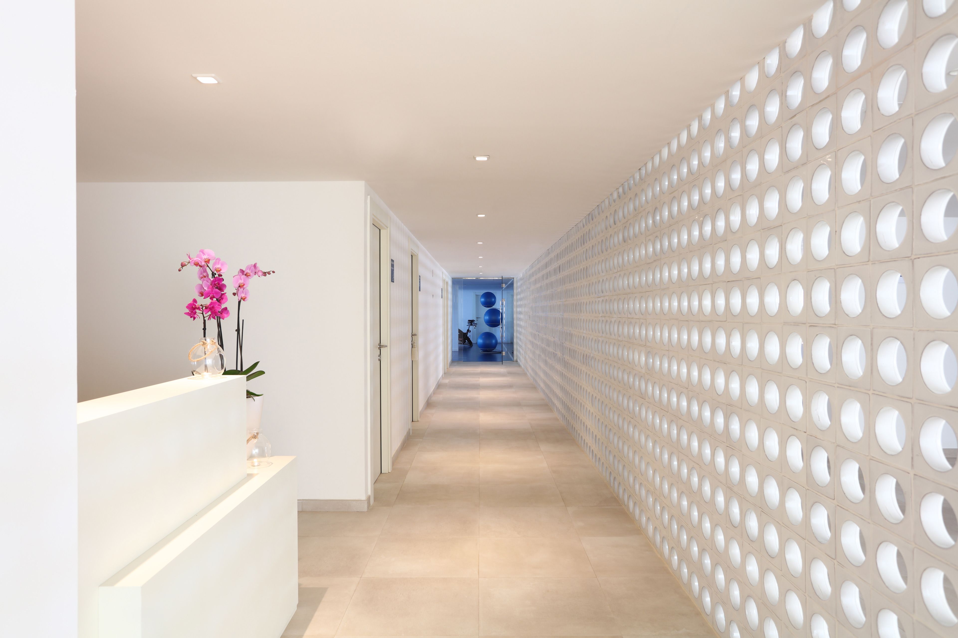 A modern hallway with a white reception desk, pink orchids, and a patterned wall with circular cutouts.