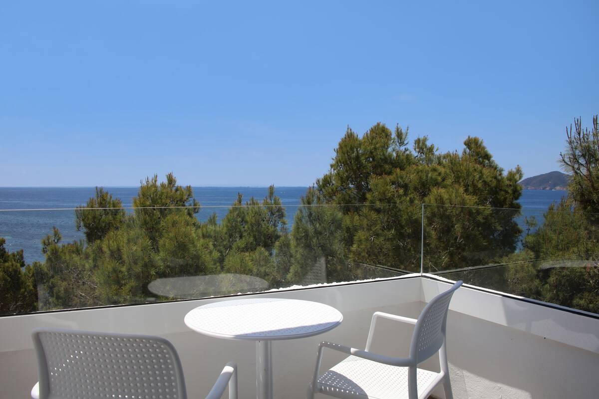A balcony with a table and two chairs, overlooking a body of water and trees.