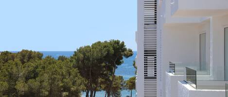 A modern building with a balcony overlooking a coastal area with trees and the sea.