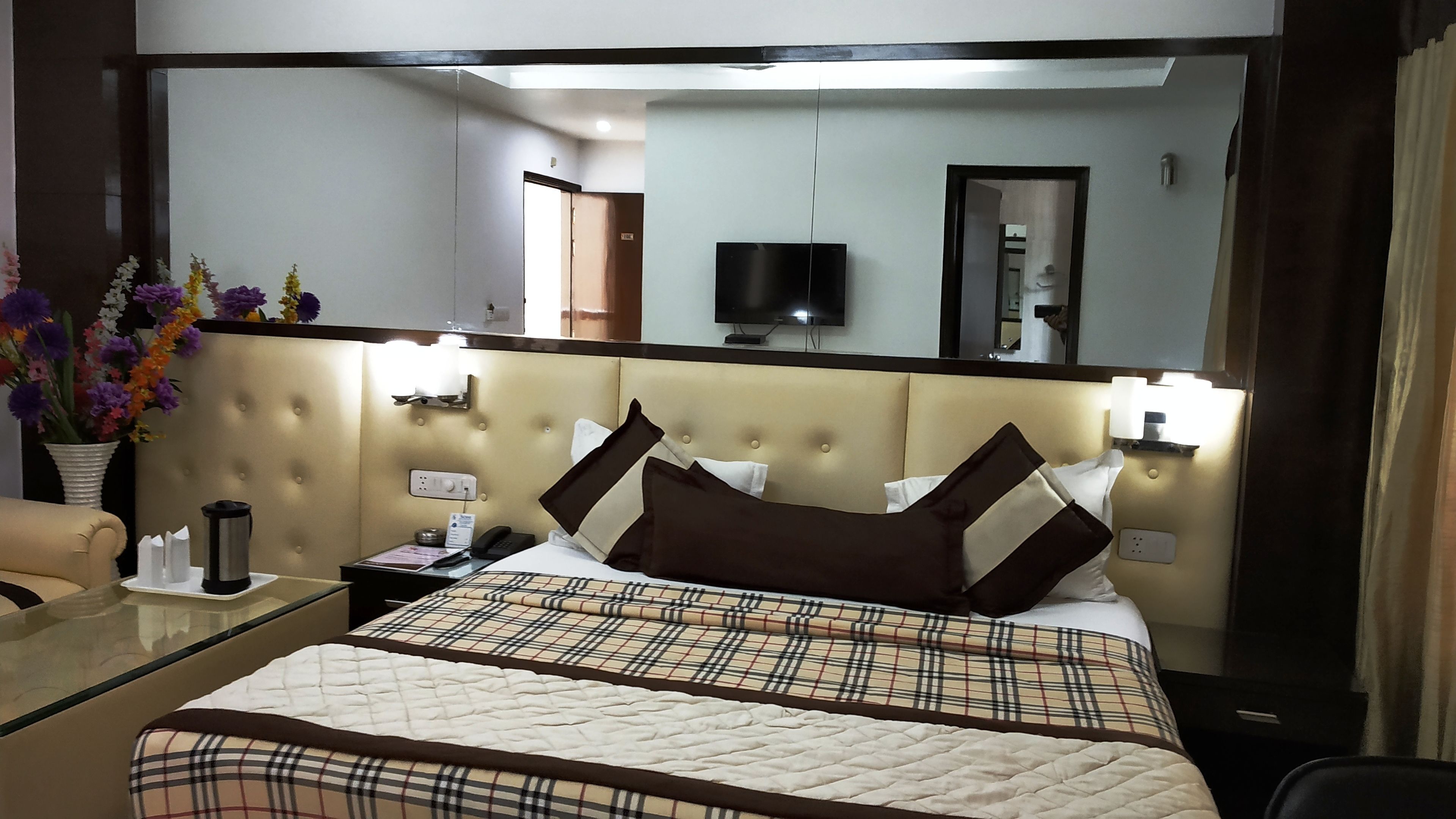 Quarto de hotel com uma cama grande, mesa de cabeceira com abajur, televisão e espelho.