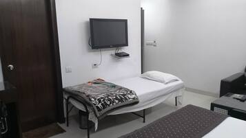 A small, clean room with a bed, a TV mounted on the wall, a desk, and a door.