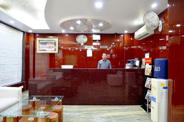 Zona de recepción de hotel con mostrador de mármol, un cuadro enmarcado y un hombre detrás.