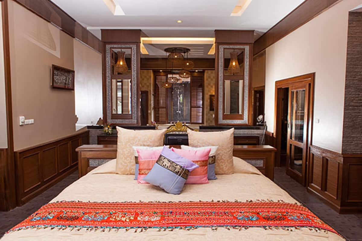 A spacious bedroom with a large bed, multiple pillows, a decorative rug, and a mirror above the bed.