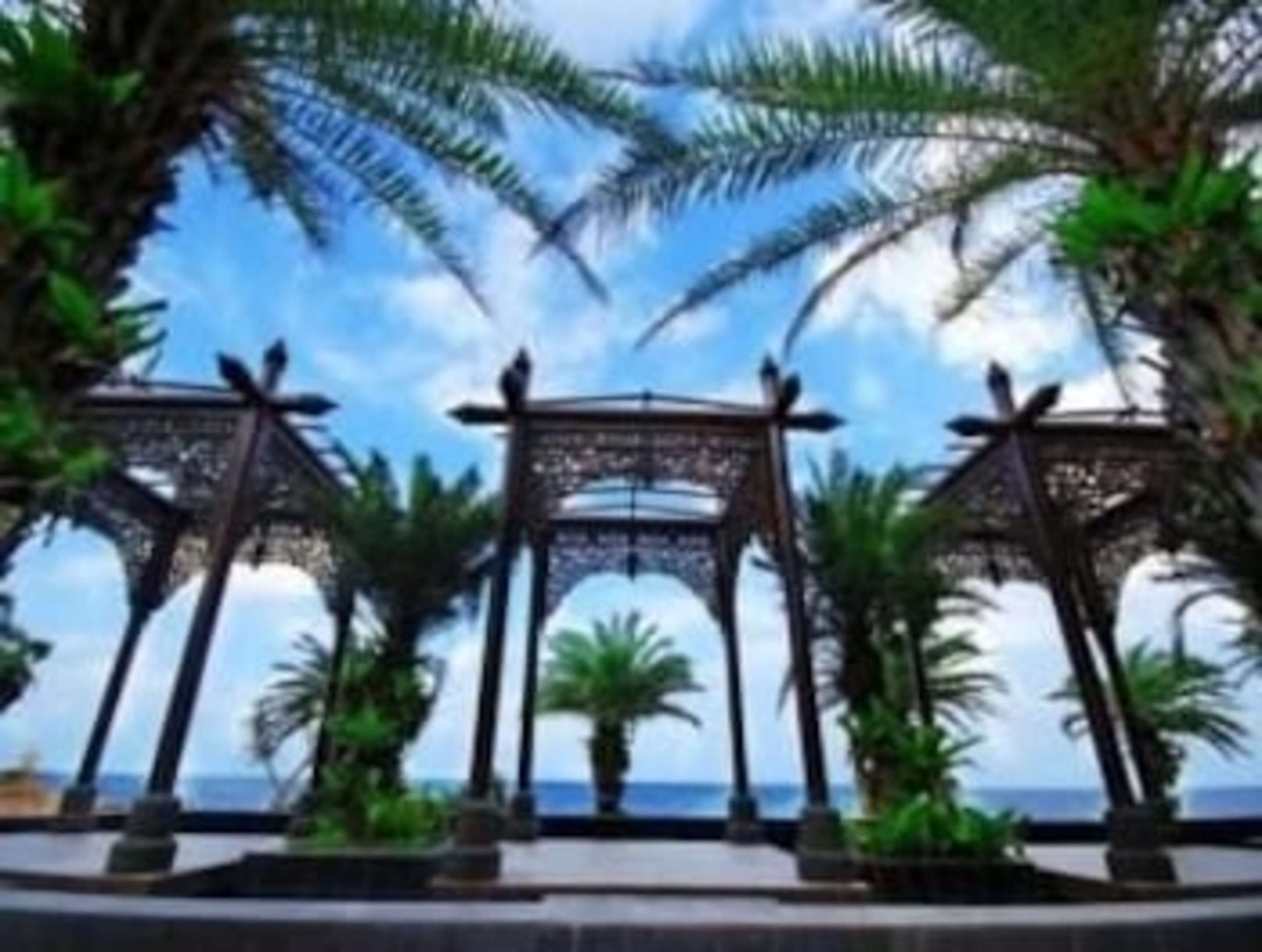 A view of a beachside walkway with palm trees and a clear sky.