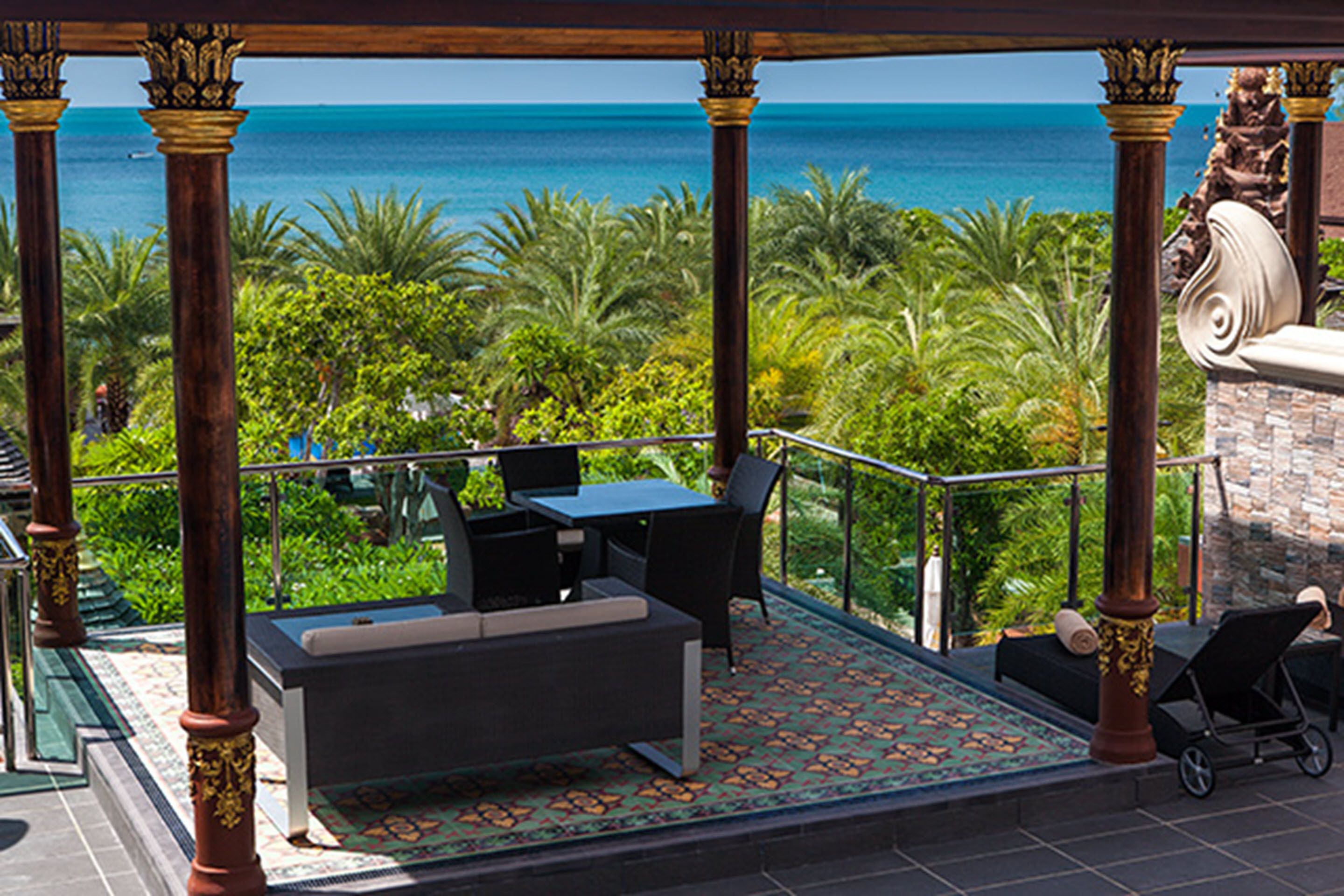 A covered outdoor seating area with a view of the ocean, featuring a table and chairs, a sofa, and a patterned floor.