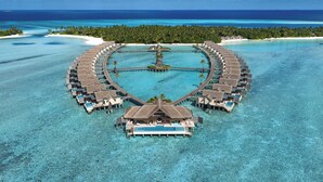 An overwater resort with circular bungalows, a central pool, and clear turquoise waters.