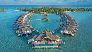 An overwater resort with circular bungalows connected by walkways, a central building, and clear turquoise waters.