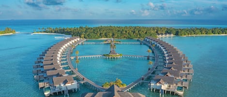 An overwater resort with circular bungalows connected by walkways, a central building, and clear turquoise waters.
