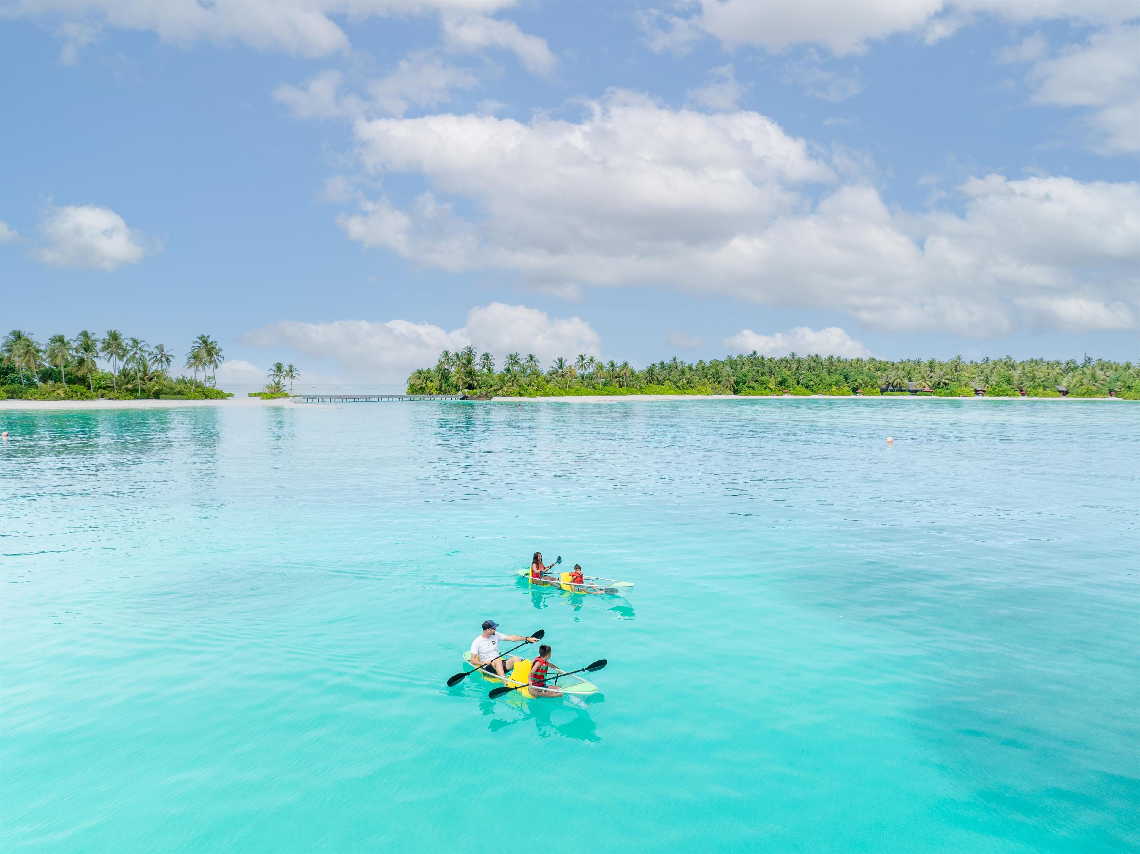 Une mer turquoise aux eaux limpides, avec une petite île qui se profile à l’horizon, entourée de palmiers.