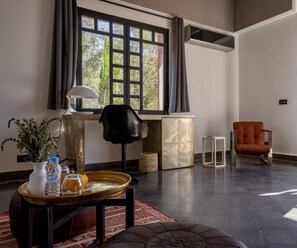 A modern living room with a large window, a black chair, an orange armchair, a small white table, and a decorative rug.