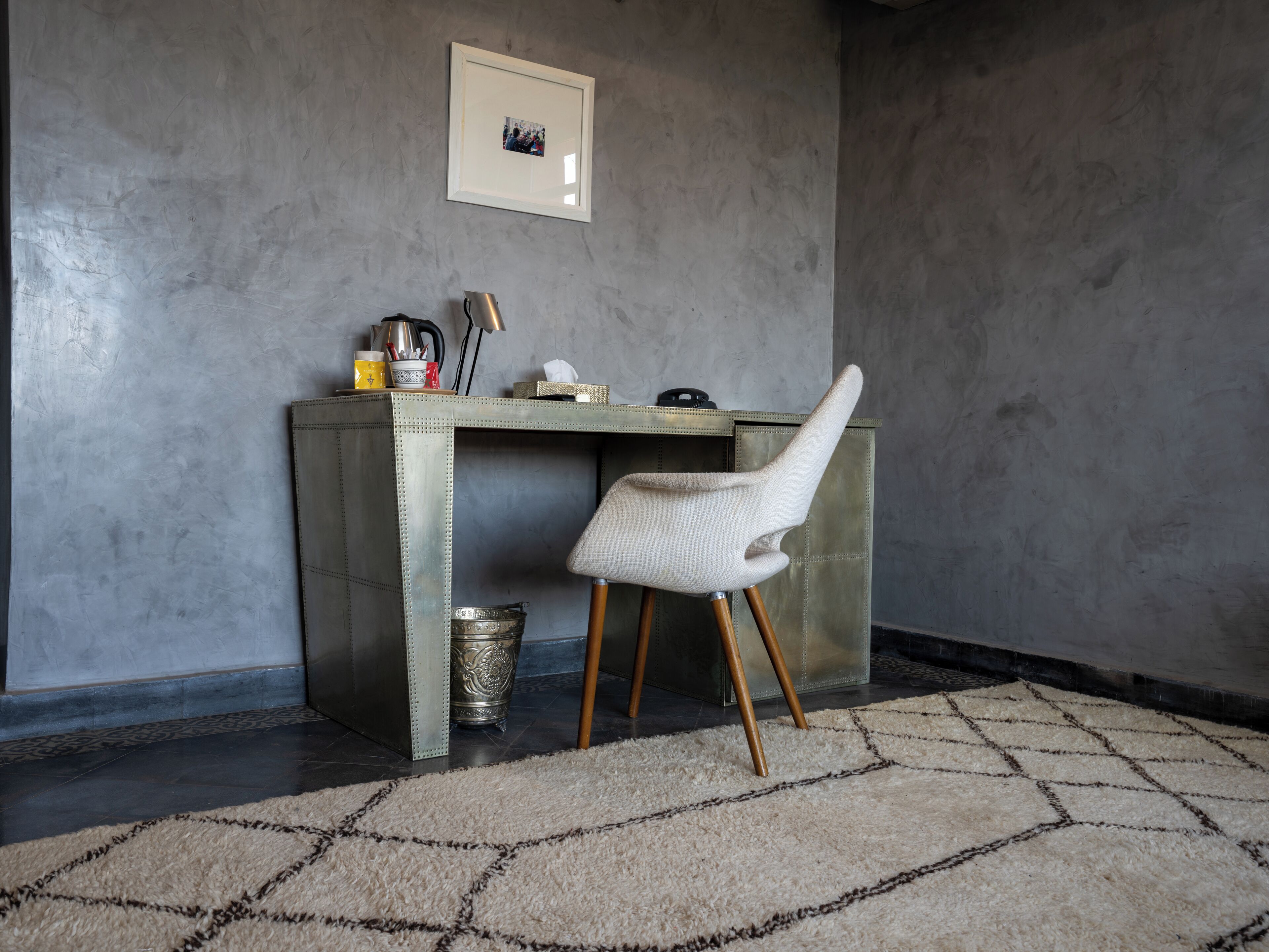 A room with a desk, chair, and a framed picture on the wall.