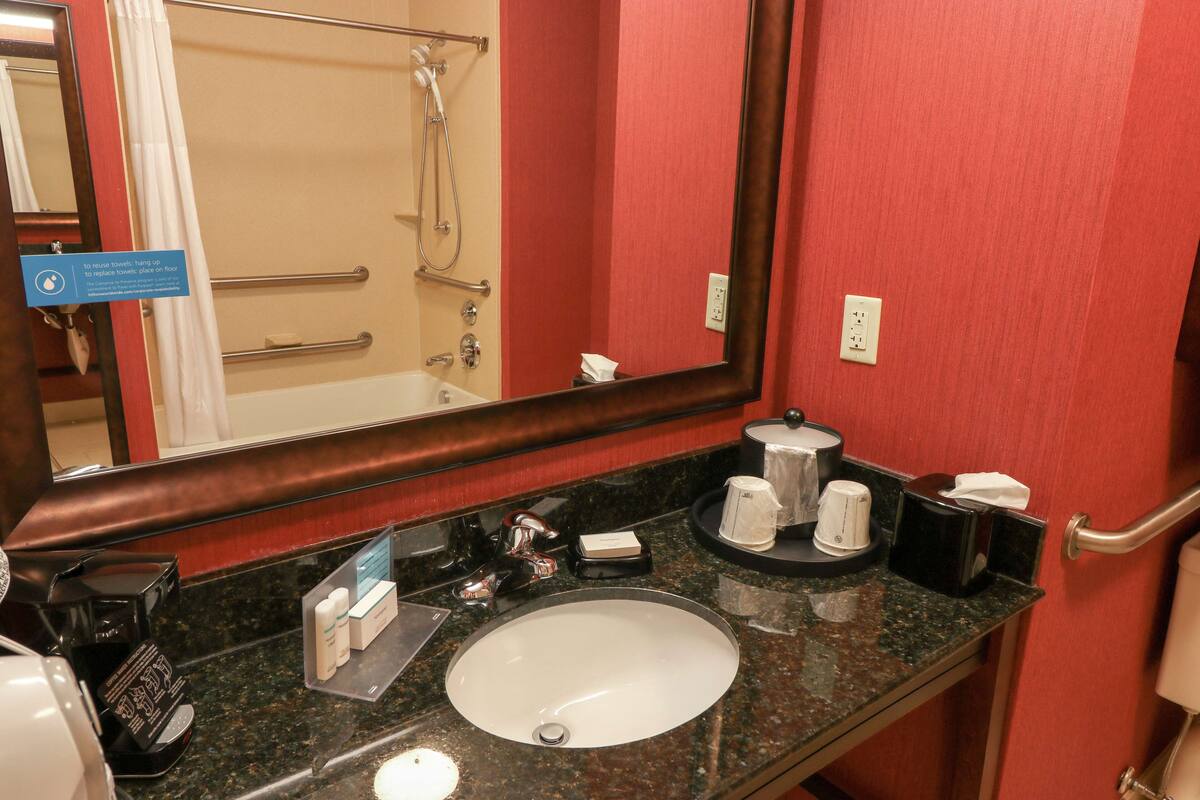 A hotel bathroom with a sink, mirror, towel rack, and a shower area.